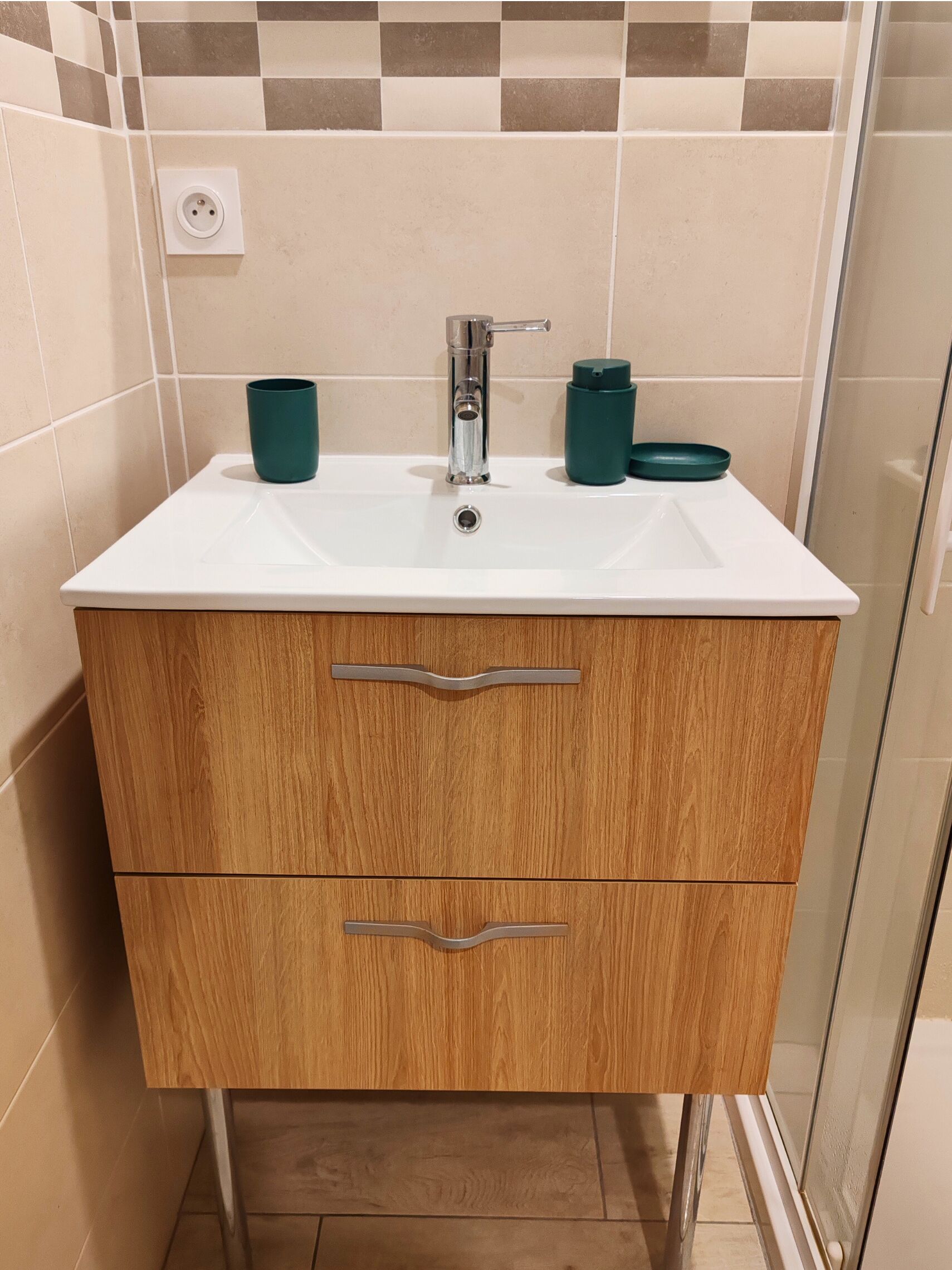 Un baño con un lavamanos blanco, dos cajones de madera y una cabina de ducha de cristal.