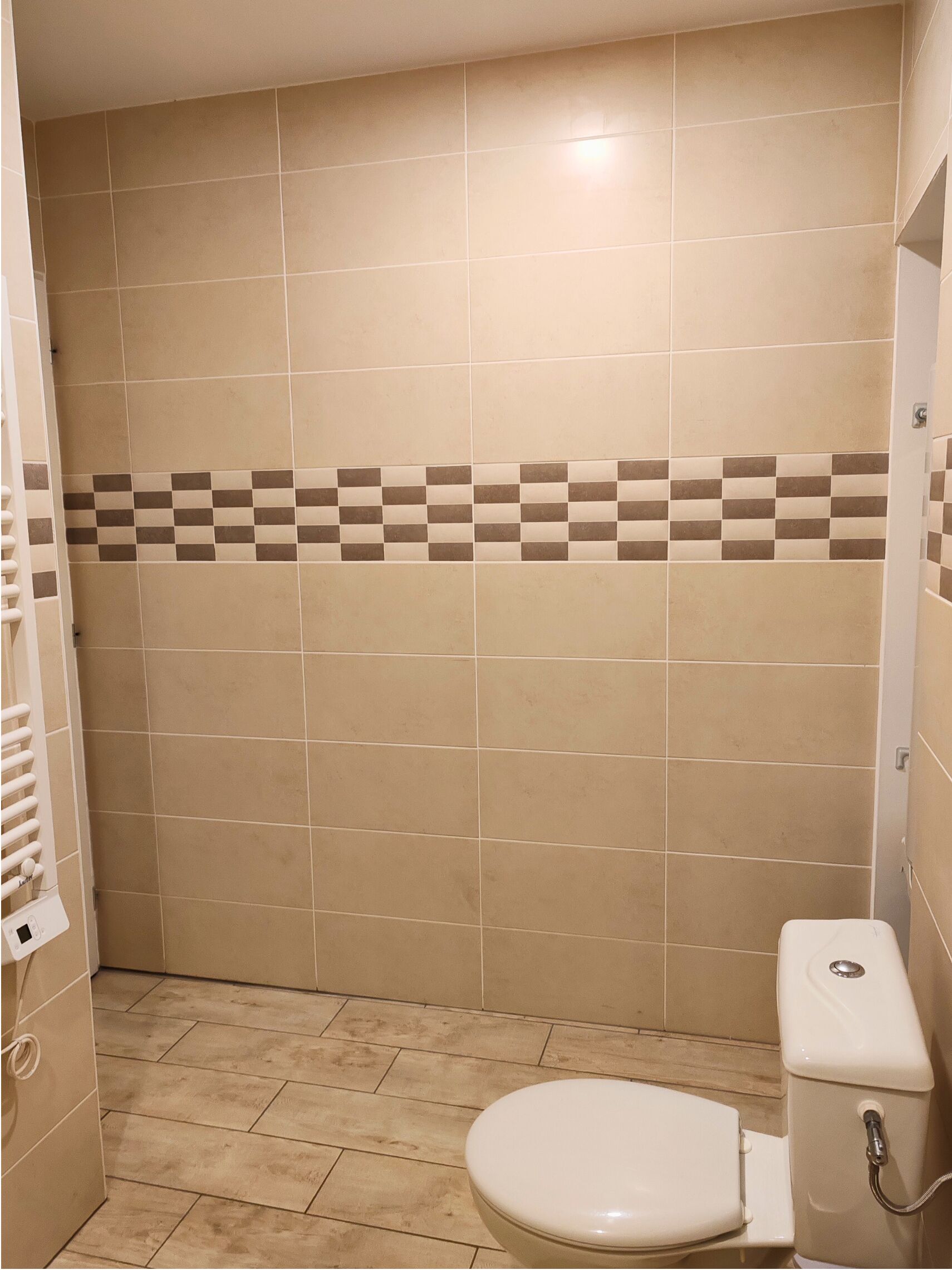 A bathroom with beige tiles, a checkered tile border, a toilet, and a towel rack.