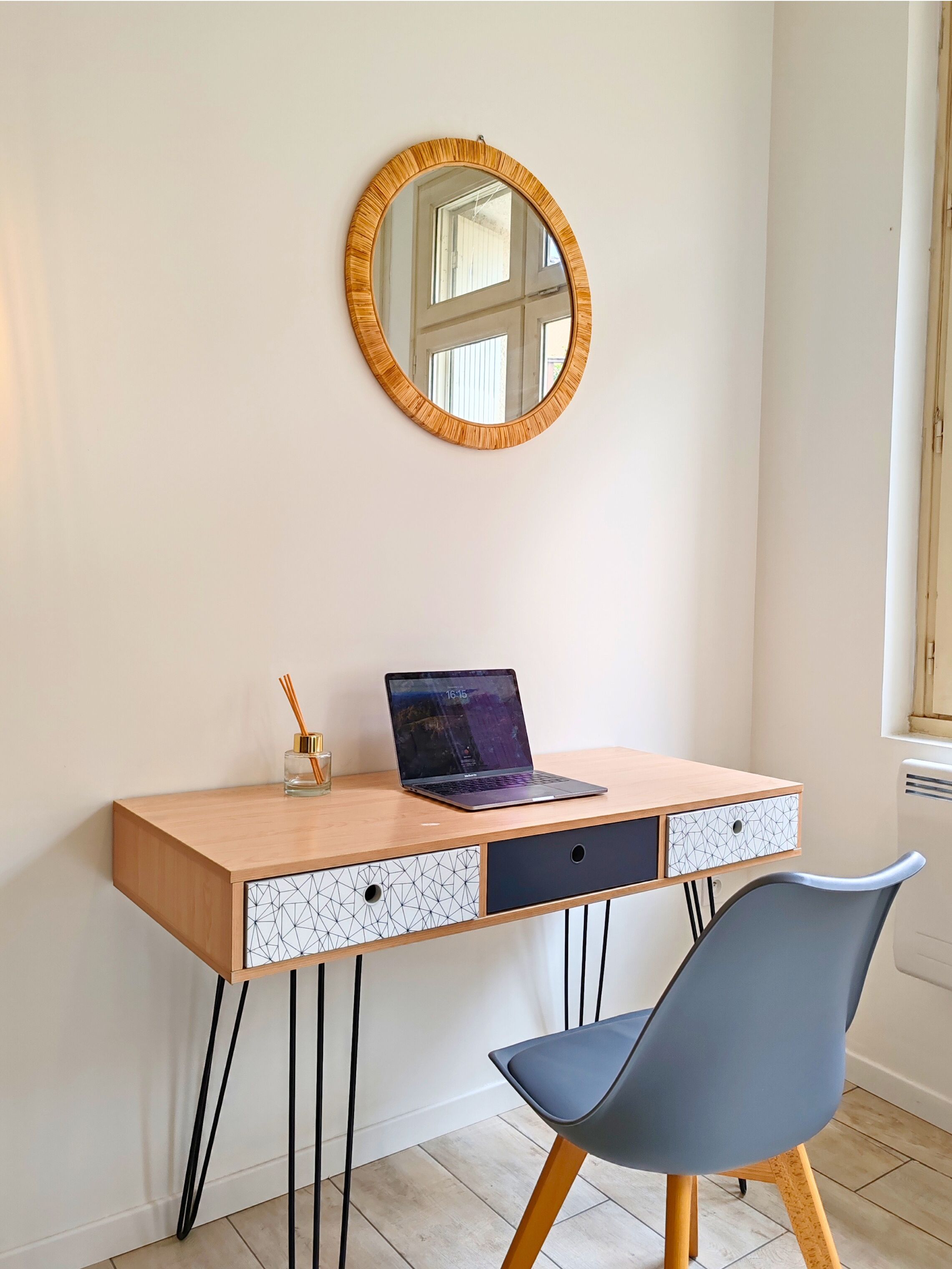 Een houten bureau met een laptop, een spiegel en een stoel in een kamer met een raam.