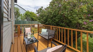 Een houten terras met een bank, stoelen, een kleine tafel en een leuning.