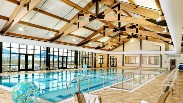 An indoor swimming pool with a high ceiling and wooden beams, surrounded by lounge chairs and a large decorative ball.