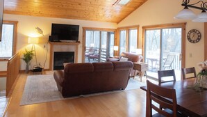 A spacious living room with a fireplace, wooden ceiling, and large windows.