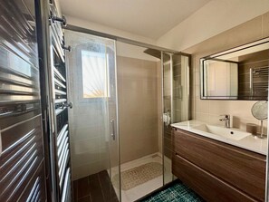 A modern bathroom with a glass shower enclosure, a wooden vanity, and a large mirror.