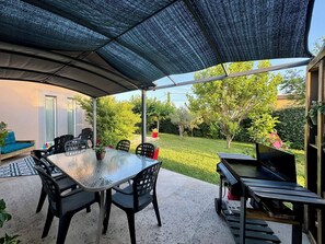 An outdoor patio with a round table and chairs, a grill, and a covered area with a mesh roof.