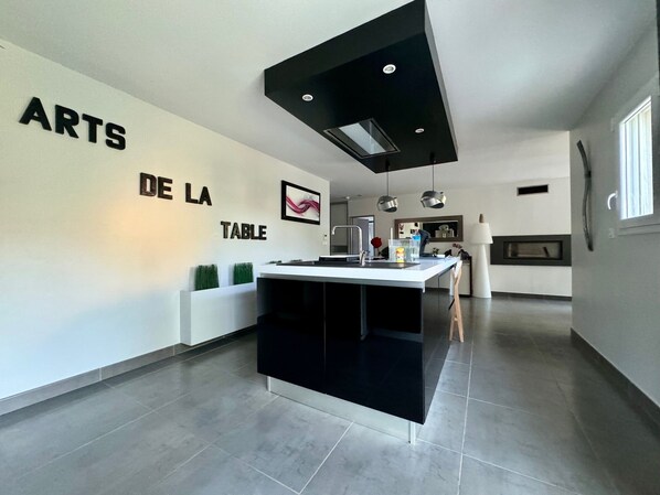 A modern kitchen with a central island, a black ceiling vent, and a wall-mounted sink.