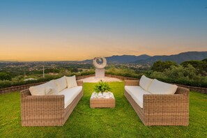 Un espace extérieur aménagé avec des meubles en osier, comprenant deux canapés et une table centrale, offrant une vue panoramique sur un paysage magnifique avec des montagnes et un ciel dégagé.