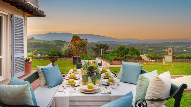 An outdoor dining area with a table set for four, surrounded by chairs with cushions, a view of the countryside, and a tablecloth. - Villa Lontana in Lucca (Lucca)