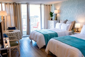 A hotel room with two beds, a desk with a chair, a dresser, and a balcony with a chair.