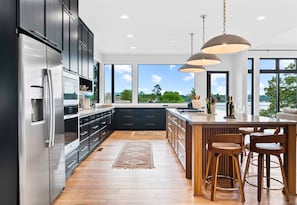 Enjoy cooking in this well-lit kitchen with a large island and bar stools, featuring a stainless steel refrigerator and sleek cabinetry.