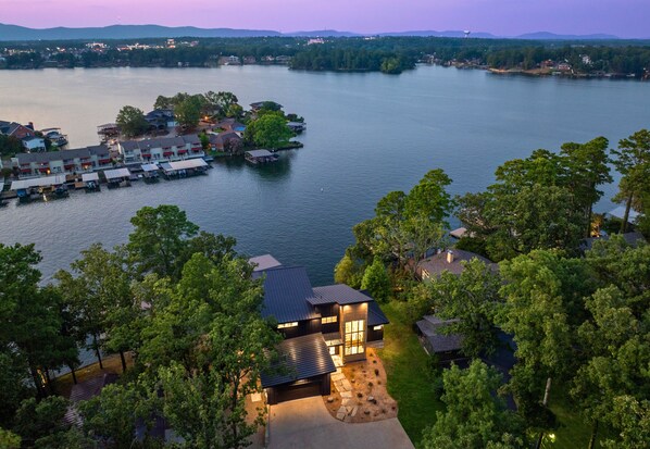 A lakeside property with a dock, a large house with a deck, and surrounding trees.