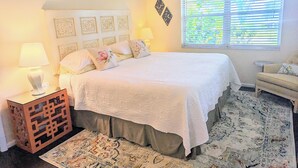 Un dormitorio con una cama, una mesita de noche, una lámpara, una ventana con persianas y una silla.