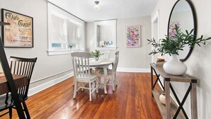 Un coin repas avec une table et des chaises blanches, un plancher en bois, un miroir et une affiche encadrée accrochée au mur.
