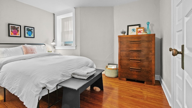 Une chambre à coucher avec un lit, une commode, une fenêtre et des œuvres d’art murales.