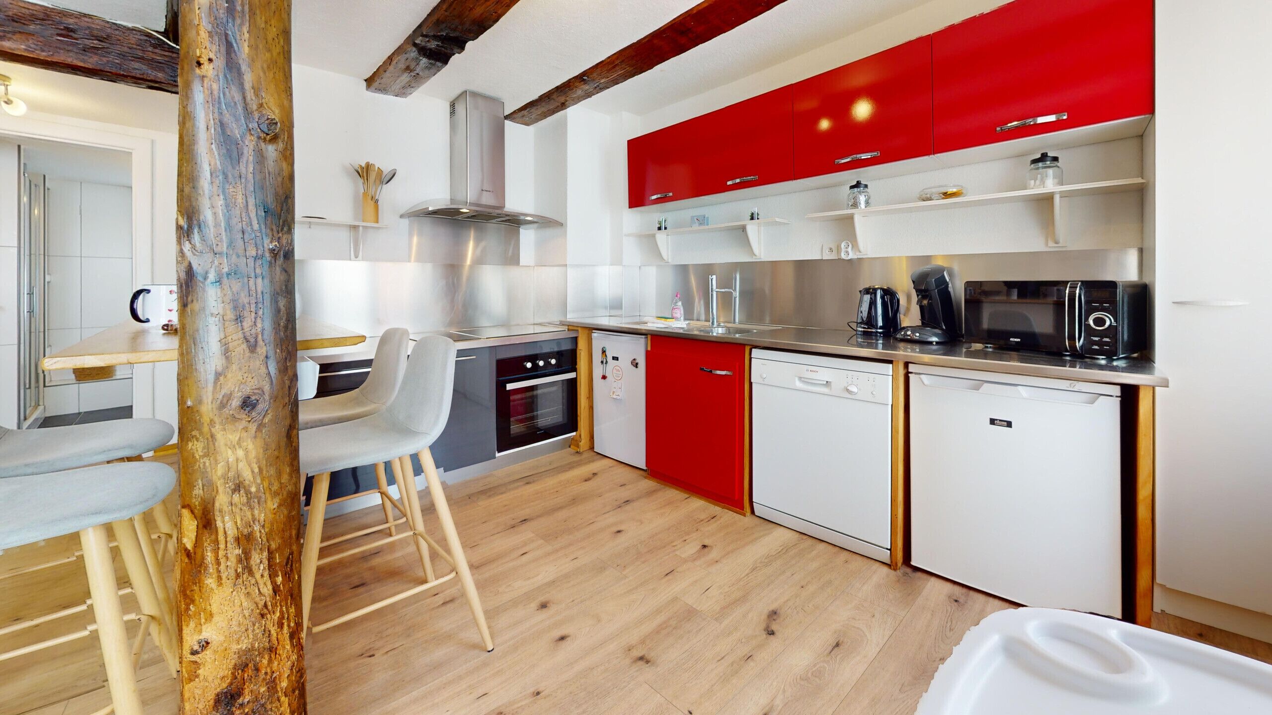 Una cocina moderna con gabinetes rojos, lavavajillas, estufa y cafetera.