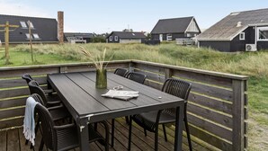 Une terrasse en bois avec une table et des chaises, donnant sur une zone herbeuse où se trouvent des maisons en arrière-plan.