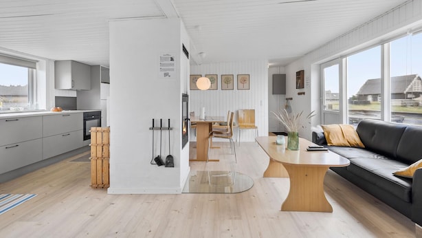 Une cuisine moderne avec des meubles gris, une table à manger en bois et un canapé en cuir noir.