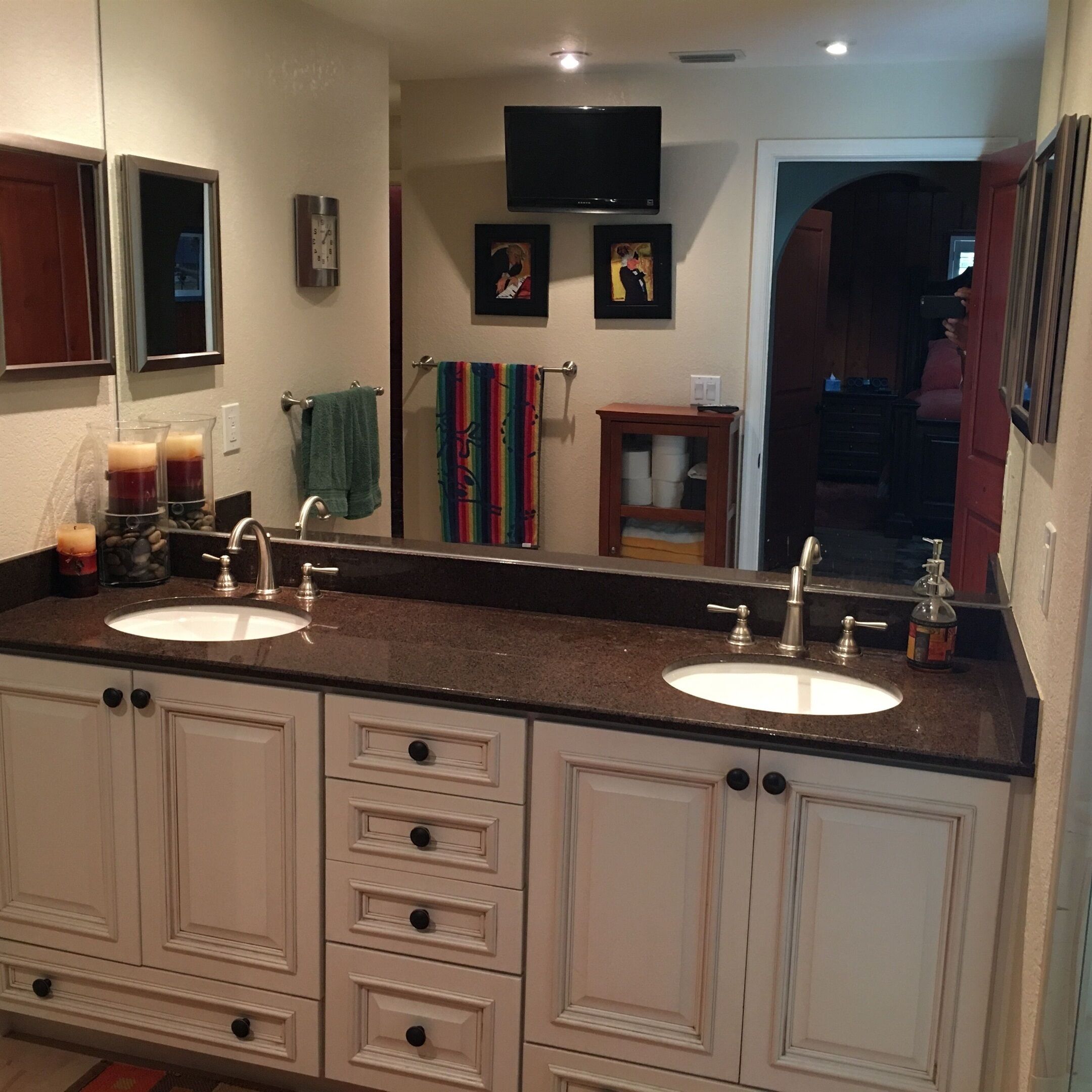 A bathroom with two sinks, a mirror, a clock, and a television mounted on the wall.