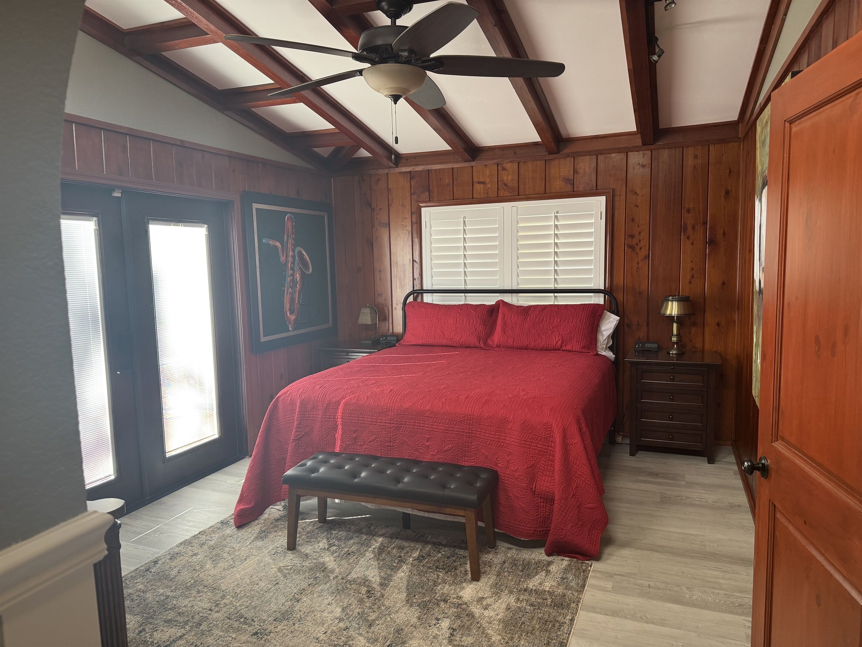 A bedroom with a bed, a bench, a nightstand, a ceiling fan, and wooden walls.