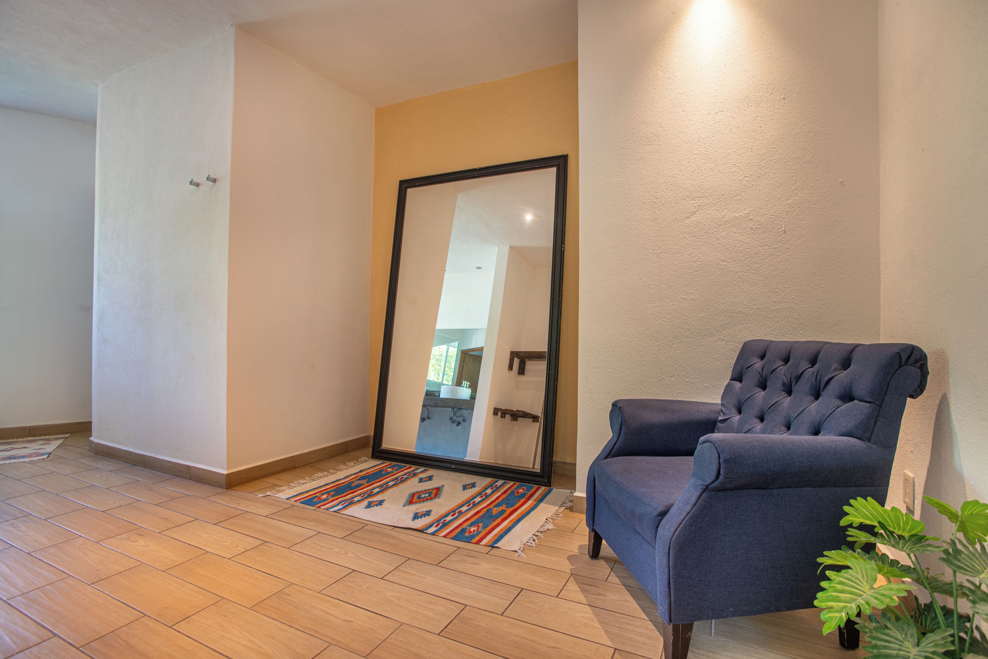 A room with a large mirror, a blue armchair, a patterned rug, and a potted plant.
