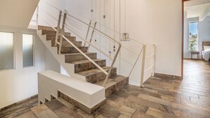 A modern staircase with wooden steps and a white handrail, leading to a room with a large window and a view of the outdoors. - LUXO Villa Acapulco Zona Brisas Guitarrón (Acapulco)