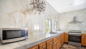 A modern kitchen with a marble countertop, stainless steel appliances, wooden cabinets, and a large window. - LUXO Villa Acapulco Zona Brisas Guitarrón (Acapulco)