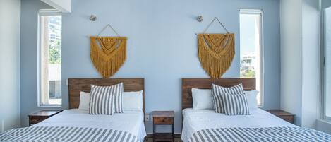 A hotel room with two beds, a wooden headboard, a small nightstand, and a macramé wall hanging.