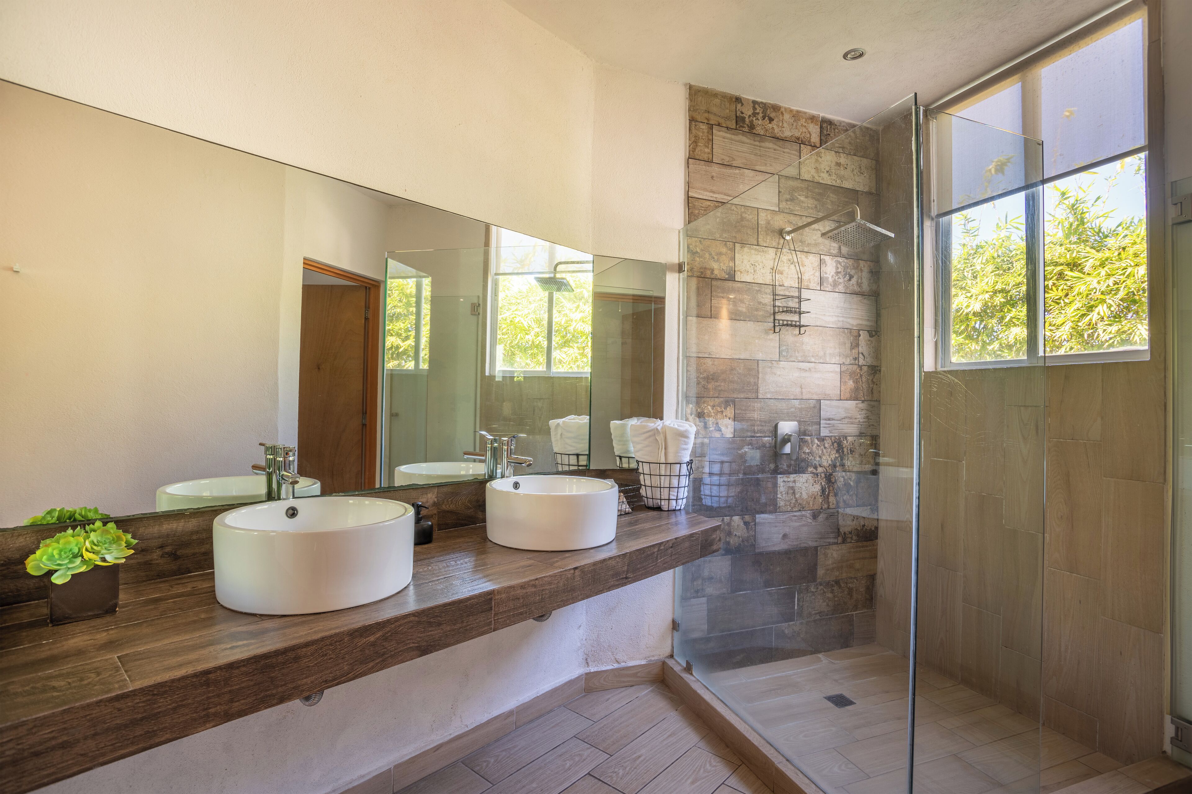 A modern bathroom with two large round sinks, a glass shower enclosure, and a large mirror.