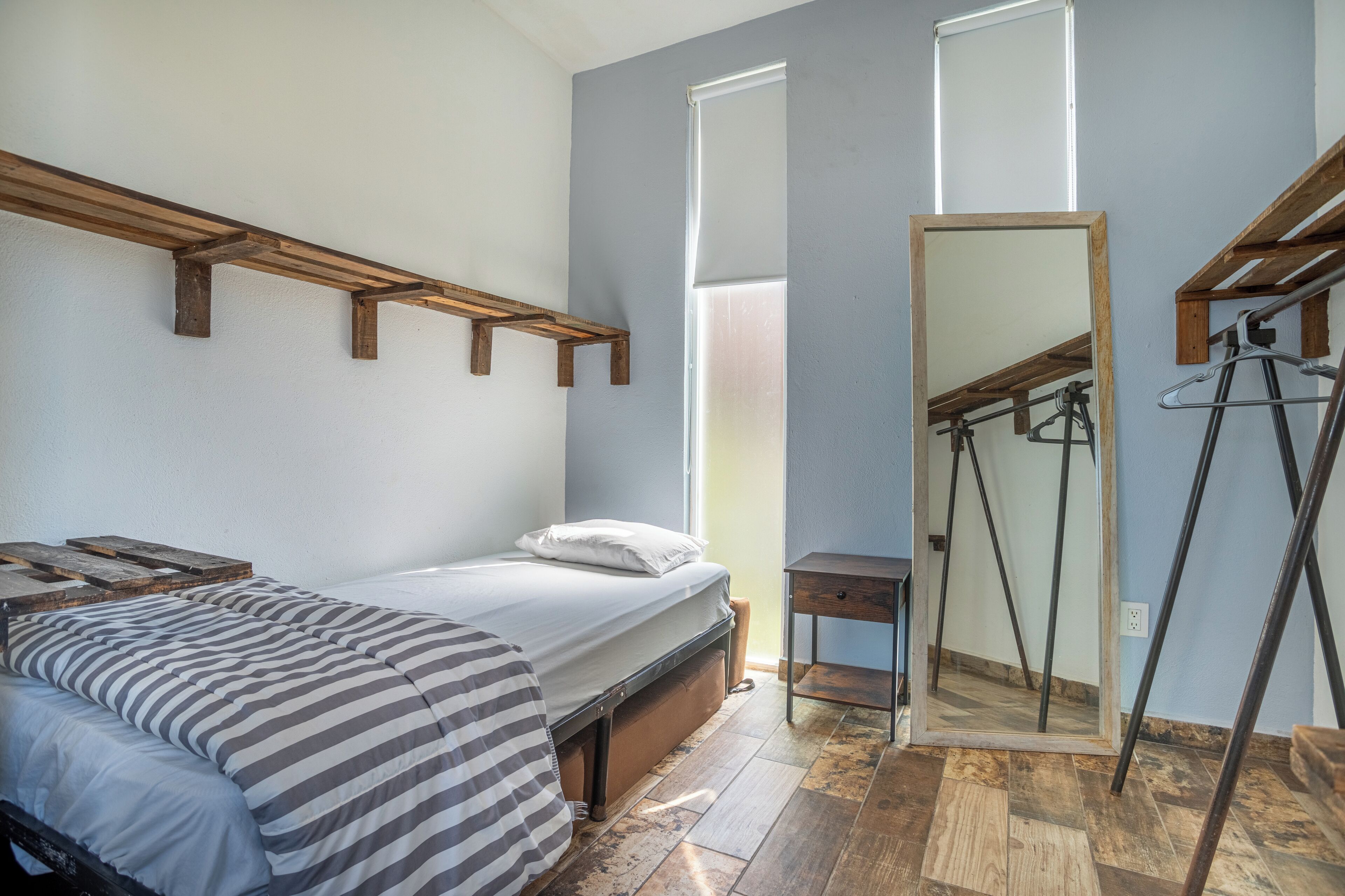 A bedroom with a bed, a wooden bench, a mirror, and a window.