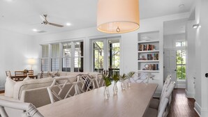Un vaste espace dédié à la salle à manger, avec une longue table en bois, des chaises rembourrées et un ventilateur de plafond.