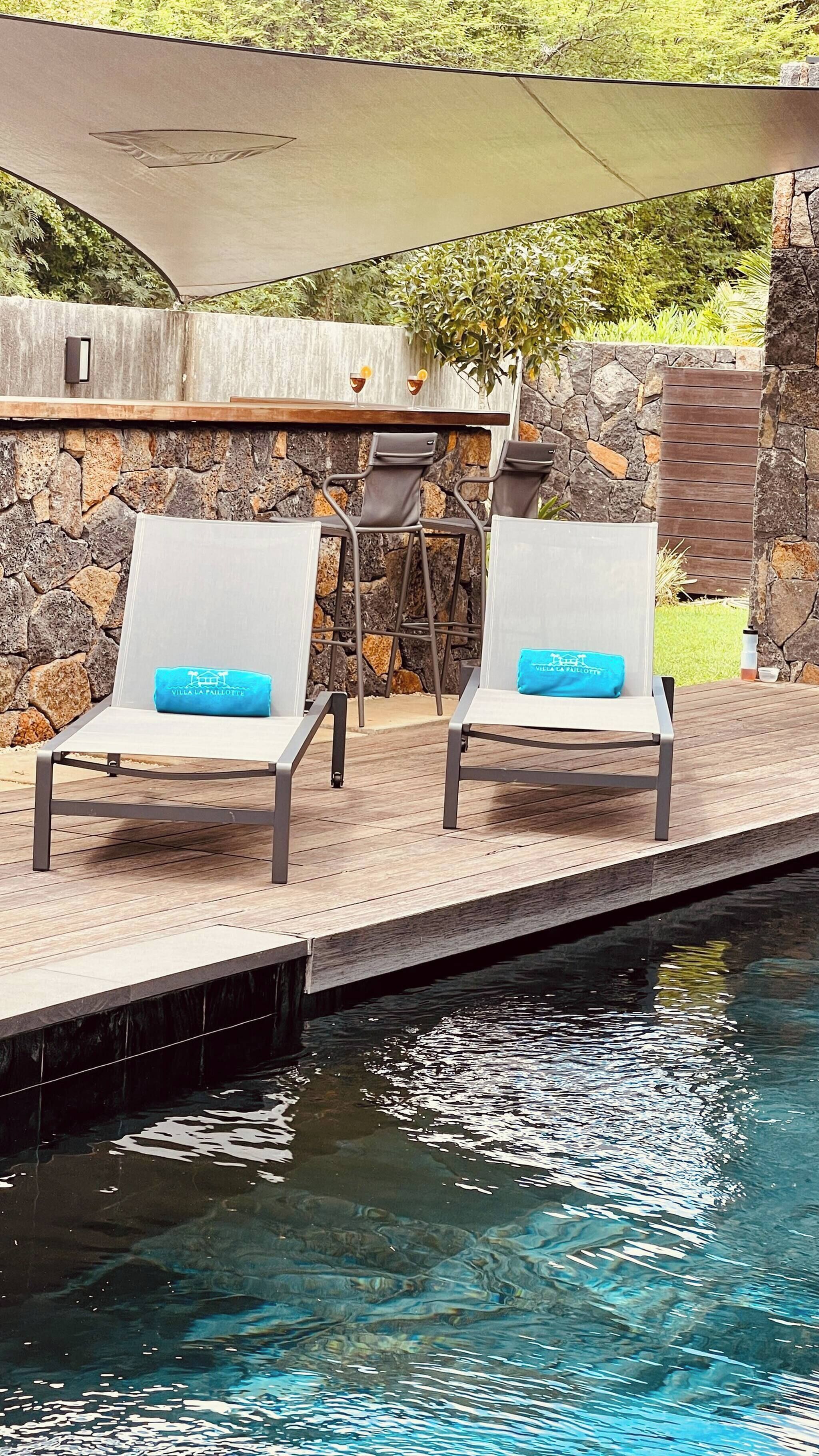A poolside area with two lounge chairs, a stone wall, and a wooden deck.