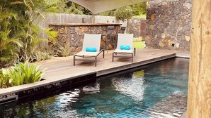 A pool area with lounge chairs and a stone wall. - Villa de Luxe La Paillotte (Black River)