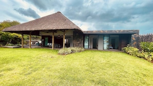 A modern house with a thatched roof structure, a stone exterior, and a well-maintained lawn. - Villa de Luxe La Paillotte (Black River)