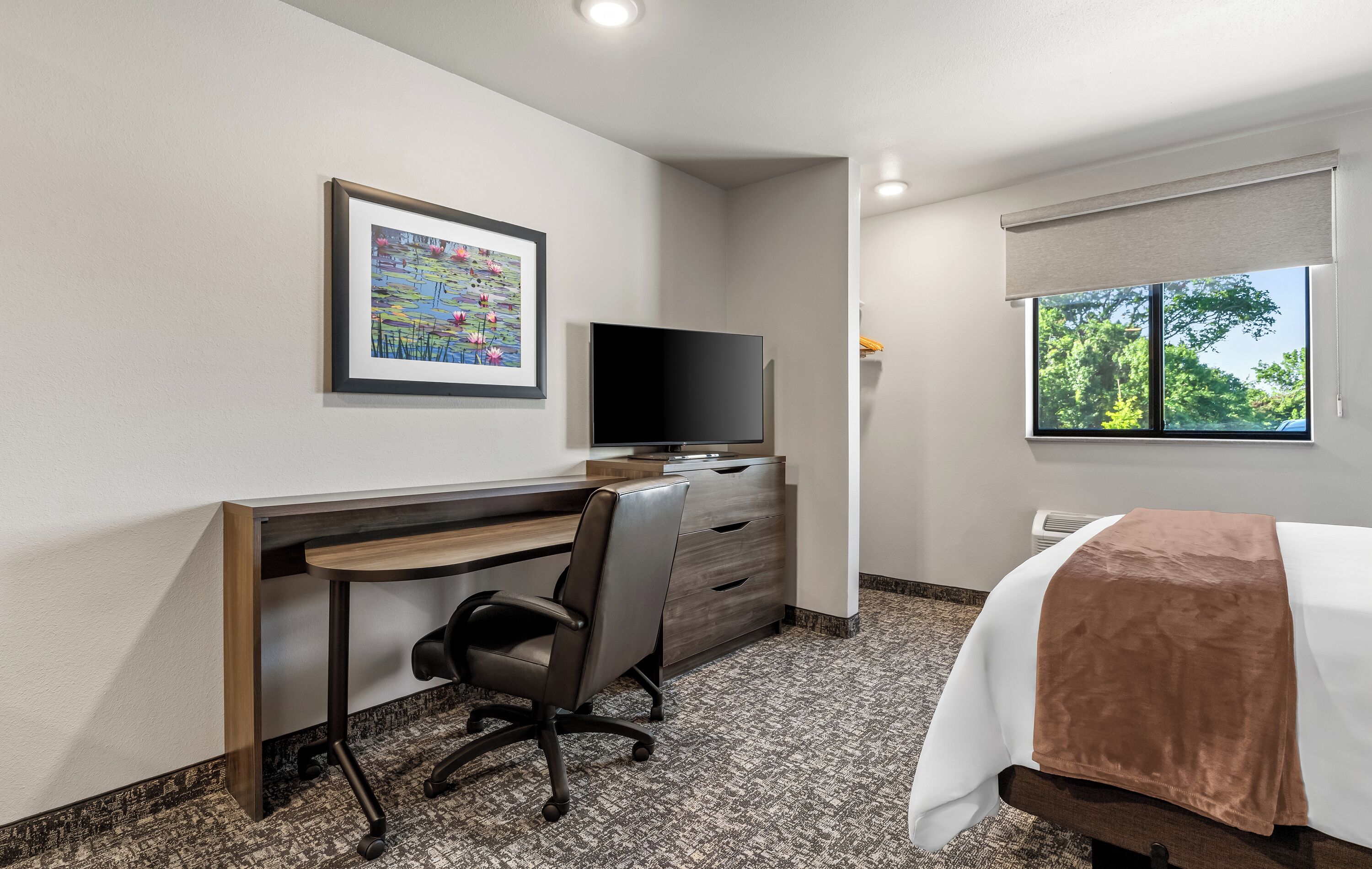 Quarto de hotel com escrivaninha, cadeira, televisão e cama com janela.