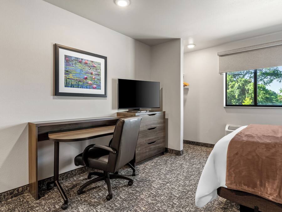 A hotel room with a desk, chair, television, and a bed with a window.