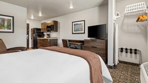 Habitación de hotel con cama, escritorio, silla, televisor, refrigerador, microondas, lavabo y tendedero.