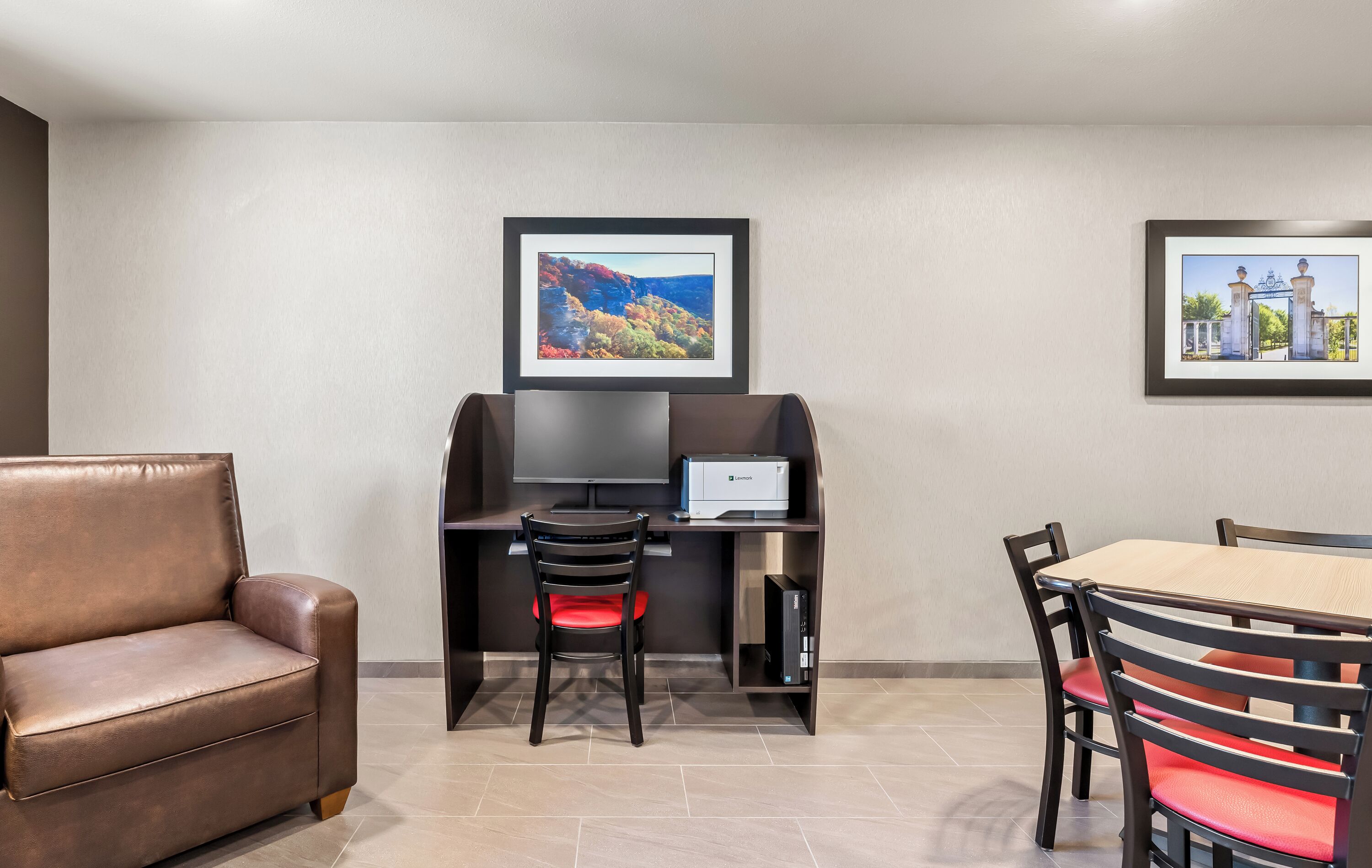 A room with a sofa, a desk with a computer, a chair, and a dining table with chairs. There are two framed pictures on the wall.