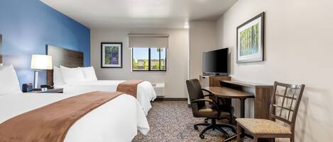 Habitación de hotel con dos camas, un escritorio, una silla, un televisor y una ventana con vistas.