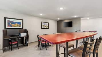 Uma sala de conferências com uma mesa comprida, cadeiras, uma TV e quadros nas paredes.