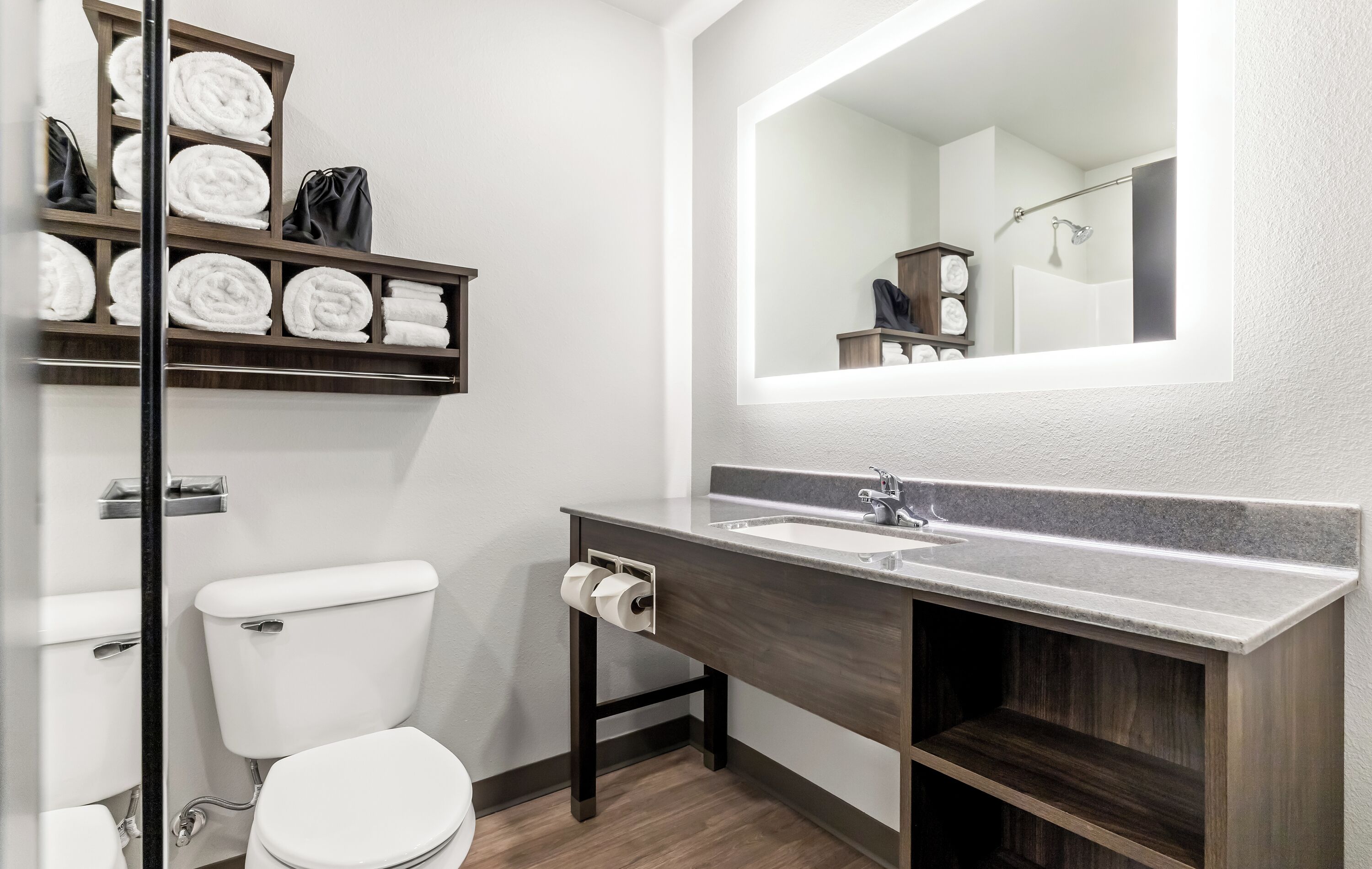 A modern bathroom with a toilet, a sink, a mirror, and a shelf with towels.