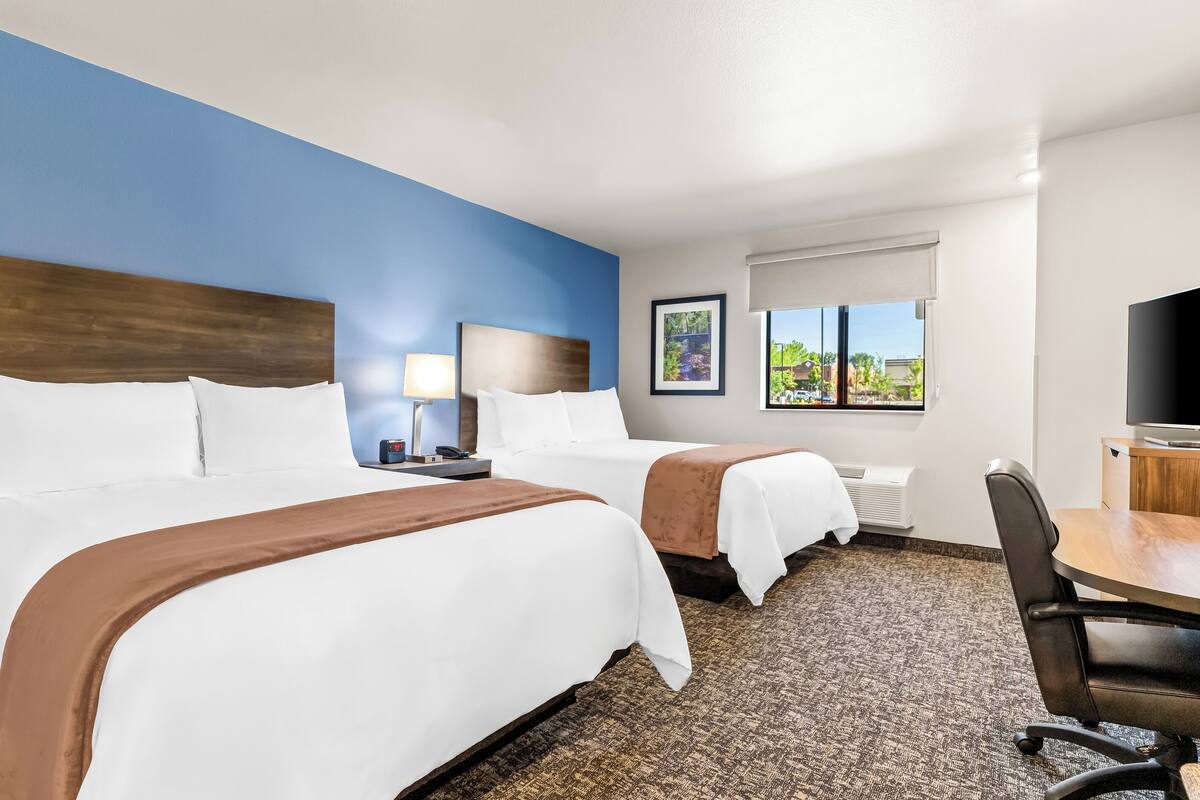 A hotel room with two beds, a desk, a chair, a TV, and a window with a view.