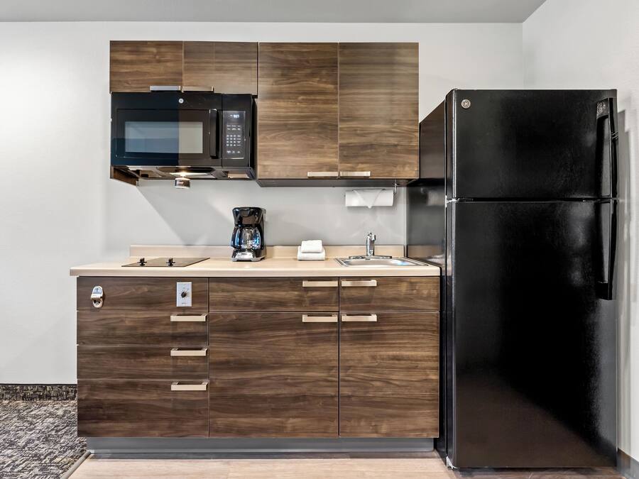 A modern kitchen with wooden cabinets, a black refrigerator, a microwave, and a coffee maker.
