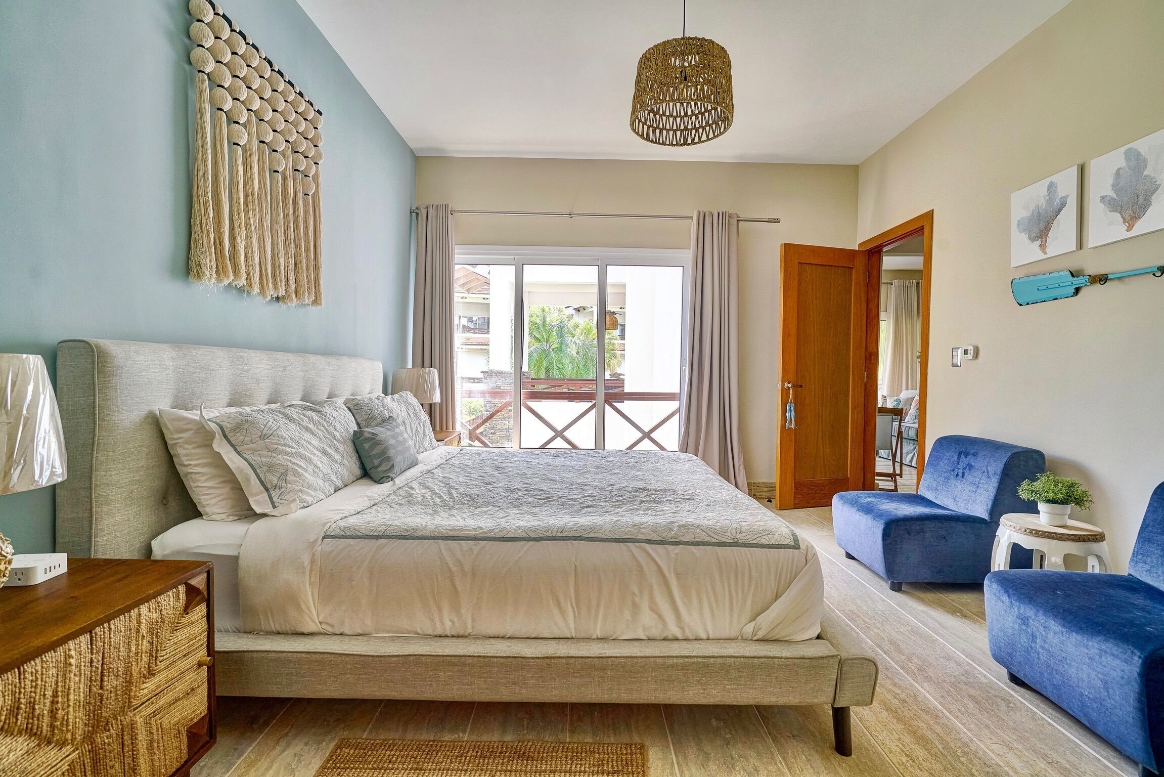 Un dormitorio con cama, una mesita de noche, una lámpara, una silla azul, un taburete pequeño y un colgador de techo.