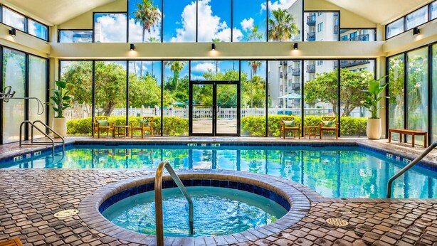 An indoor swimming pool with a hot tub, large windows, and outdoor views.