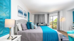 A modern bedroom with a bed, bedside table, lamp, and a view of the outdoors.