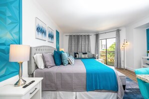 A modern bedroom with a bed, bedside table, lamp, and a view of the outdoors.