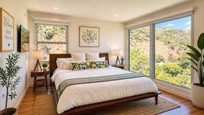 Une chambre avec un grand lit, deux tables de chevet, une commode, une fenêtre donnant sur un paysage vallonné et un panneau d’accueil accroché au mur.