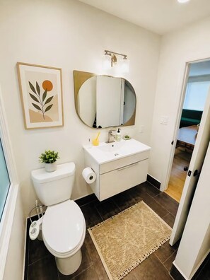 Une salle de bain équipée de toilettes, d’un lavabo, d’un miroir et d’une œuvre d’art encadrée accrochée au mur.
