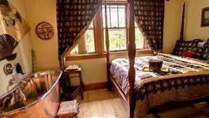 Un lit à baldaquin, un plancher en bois, une petite table et une fenêtre avec des rideaux.