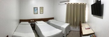 Una habitación de hotel con dos camas individuales, una mesita, un televisor y un equipo de aire acondicionado.
