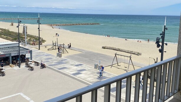 A beach view from a balcony with a railing, a café, and a lifeguard tower in the background. - Apartment with sea view, at the foot of the beach, ideal for a couple with 2 children (Saint-Cyprien)